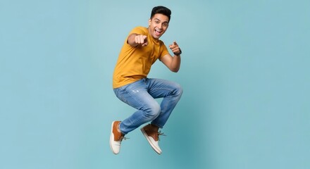 A young man with a yellow t shirt jumping and pointing at the camera on a light blue background