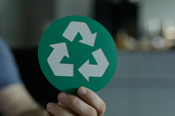Close-up of a hand holding a round green card with a white recycle symbol.  Perfect for...