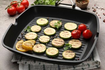 Delicious grilled courgette slices with tomatoes, lemon and parsley in pan on grey textured table,...