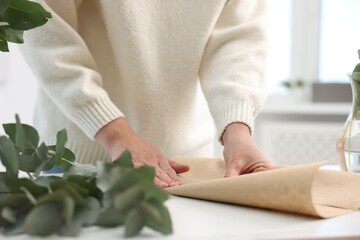 Florist making beautiful bouquet of eucalyptus branches at white table in flower shop, closeup