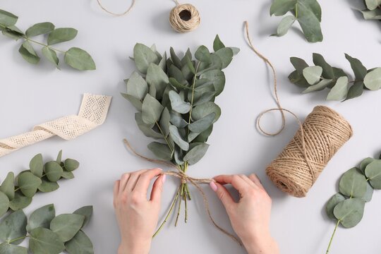 Florist making beautiful bouquet of eucalyptus branches at white table, top view