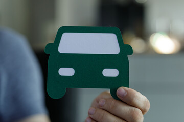 Close-up of a hand holding a green paper cutout of a car.  Perfect for automotive, insurance, or transportation concepts.