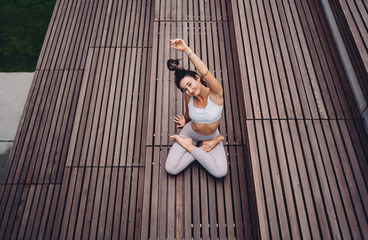 Young woman practicing seated yoga stretch in lotus pose, one arm raised. Conceptual image...
