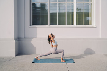 Focused woman practicing yoga lunge stretch on mat, arms interlaced behind head. Conceptual stock...