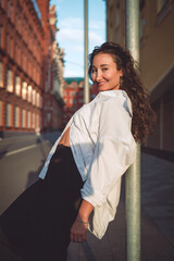 Smiling woman leans on pole in urban street, radiating confidence. Conceptual stock photo...