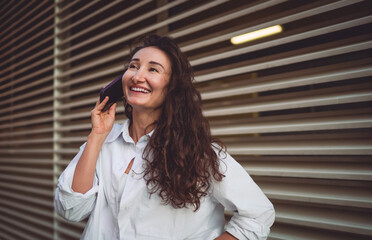 Smiling woman in white shirt talks on smartphone outdoors. Conceptual portrait symbolizing...