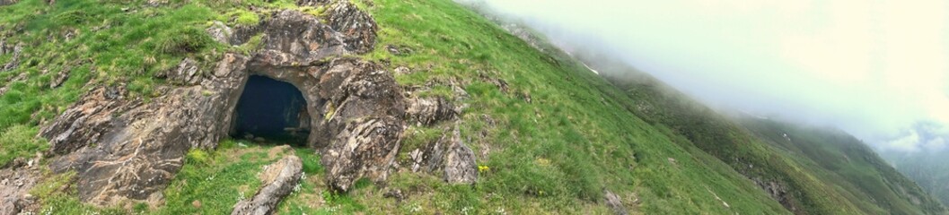 Panoramic view of a mountainside with rock formations and a cave entrance
