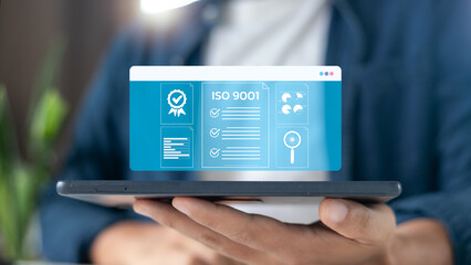 Businessman holding a tablet with an ISO 9001 certification hologram, symbol of quality management system, business standard, corporate excellence, compliance, and international certification.
