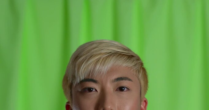  Close-up video clip of a young adult male pondering and smiling in the studio, looking from side to side, his face partially obscured. He has bleached hair and is wearing casual clothing.