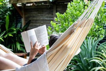 Person relaxing in a hammock reading a book surrounded by lush greenery in a tranquil outdoor...