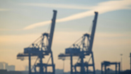 Obraz premium Two cranes stand against a bright sky in a harbor or industrial area, forming strong vertical lines and industrial silhouettes that dominate the shipping landscape.