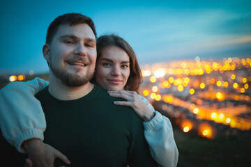 Young family couple embracing on hilltop overlooking city lights at dusk © KONSTANTIN SHISHKIN