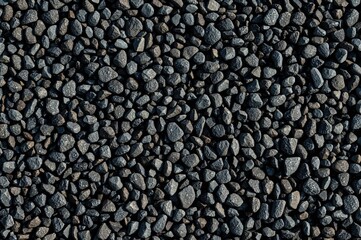 Texture of small gray stones on a white backdrop. Dark gravel and pebbles surface close-up. Crushed granite with clay aggregation under dark lighting.