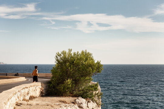 Corniche Kennedy de Marseille dans un virage avec vue sur la mer, un pin maritime, le ciel bleu et un homme vue de dos faisant de la course &agrave; pieds, Marseille, Sud de la France
