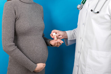 Male gynecologist giving pills to pregnant woman during appointment at colored background. Visit To...