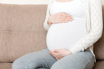 photo of cute caucasian future mom lying in light living room on sofa and holding hands on tummy