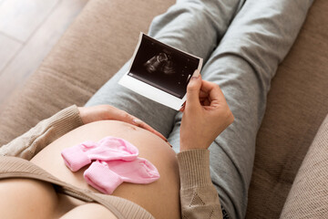 Pregnant Woman sitting on bed and Looking At Ultrasound Scan photo of her Baby. A pregnant female...