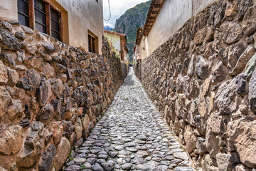 Traditional narrow alleyway with ancient Inca stone walls and cobblestone pavement in the historic town of Ollantaytambo, Peru.