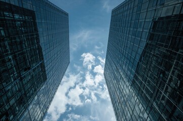 Looking up at sleek modern skyscrapers featuring reflective glass facades under a clear blue sky with ample space for text.