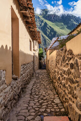 Traditional narrow alleyway with ancient Inca stone walls and cobblestone pavement in the historic town of Ollantaytambo, Peru.