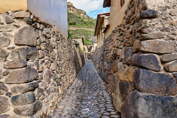 Traditional narrow alleyway with ancient Inca stone walls and cobblestone pavement in the historic town of Ollantaytambo, Peru.
