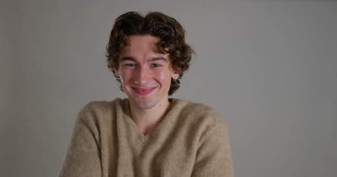  Medium video clip of a young adult male smiling directly at the camera while hugging himself in the studio. He has dark curly hair and is wearing a casual sweatshirt.