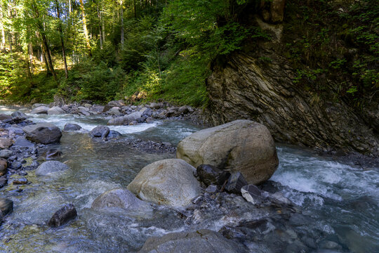 mountain river Samina in the forest in a riverbed with rocks and trees on both sides towrds blue sky in Saminatal in Vorarlberg Austria