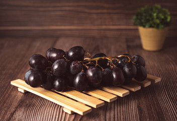 Bunch of fresh purple grapes on a black plate, placed on a wooden base, with a rustic background. Natural style image, ideal for concepts of healthy eating, fruits, nutrition and gastronomy.