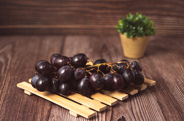 Bunch of fresh purple grapes on a black plate, placed on a wooden base, with a rustic background. Natural style image, ideal for concepts of healthy eating, fruits, nutrition and gastronomy.