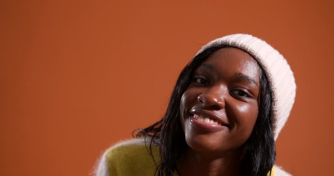 Video clip of a young adult female walking towards the camera in the studio, smiling and moving from side to side when she is close to the lens. She is wearing a woollen sweatshirt and beanie.