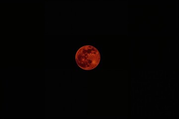 Bright crimson lunar orb against pitch-black night, captured with an ultra-telephoto lens from the ground.