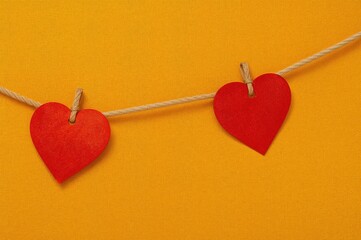 Red heart shapes hanging on a string against a bright yellow backdrop