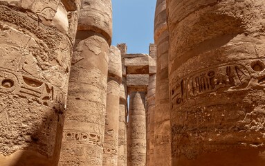 Egyptian columns with intricate hieroglyphics at the Karnak Temple in Luxor under a bright blue sky