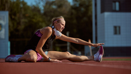 Female athlete stretching on track on a sunny day training session outside. Concept of motivation, training dedication, stretching, performance readiness.