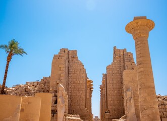 Ancient Egyptian ruins at Karnak Temple under a clear blue sky with a palm tree in Luxor, Egypt