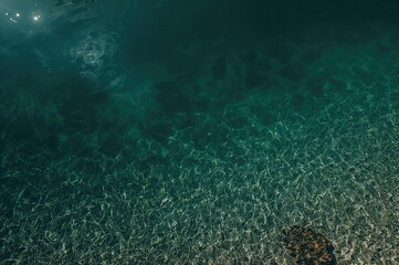 Aerial drone perspective capturing a mountain lake with vivid green water mirroring nearby peaks. Crystal-clear water over a sandy base forming a gradient appearance.