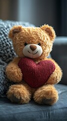 Obraz premium Cute teddy bear plush holding a red knitted heart photo on a couch