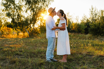 A couple embraces and shares a kiss in a tranquil field at sunset, surrounded by warm light and...