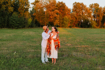 A couple shares a tender embrace in a grassy field, surrounded by trees, as the sun sets in the...