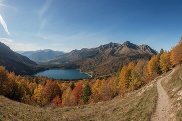 Fototapeta premium Wide view of a mountain range with a lake and autumn trees, perfect for hiking and nature exploration