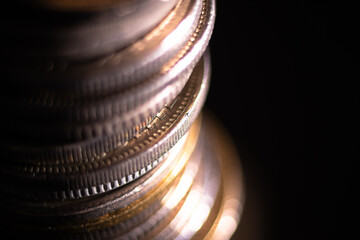 Column of coins close up against dark background, coins shine on light