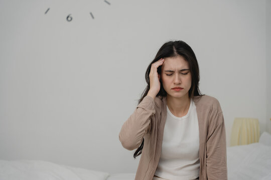 Young woman sitting on sofa holding her head in pain, showing signs of headache, migraine, or stress. Perfect for health topics, tension, fatigue, burnout, or mental health awareness content.