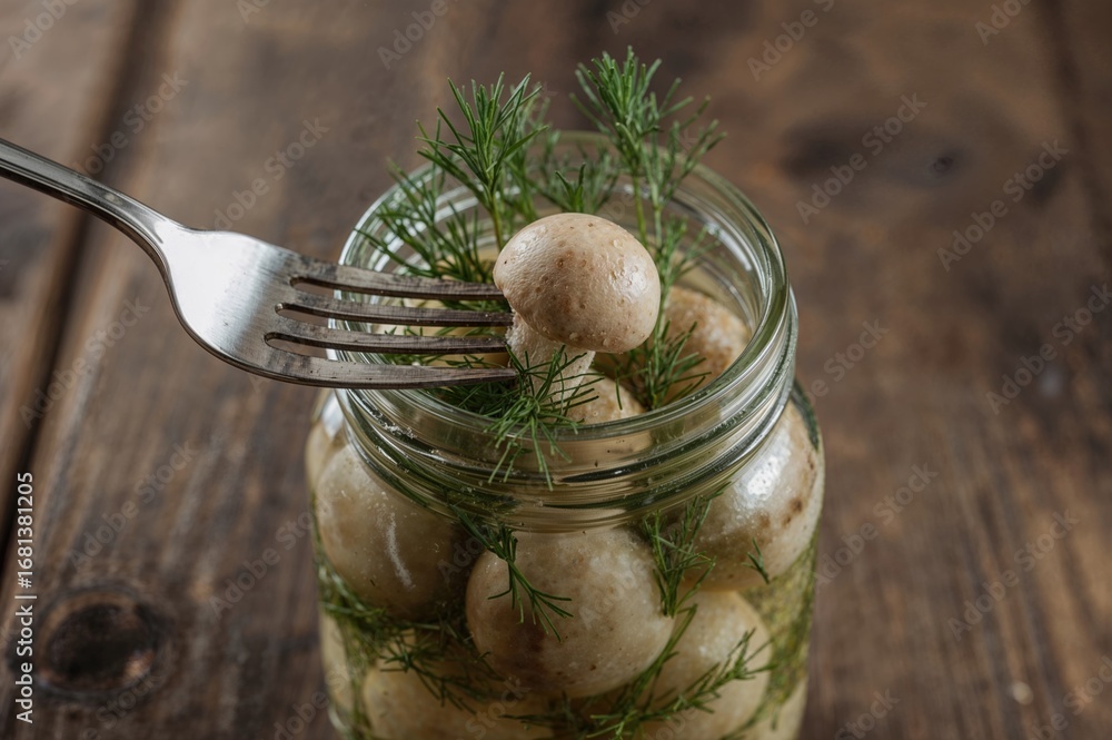 Poster close-up of a fork holding a pickled mushroom above a jar filled with boletus and dill, placed on a 