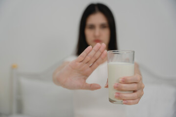Woman refusing a glass of milk with hand gesture, showing dairy allergy or lactose intolerance....