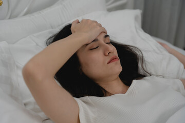 Sick woman lying in bed with eyes closed and hand on forehead, showing symptoms of headache or fever. Concept of illness, stress, fatigue, flu, migraine, and needing rest at home.
