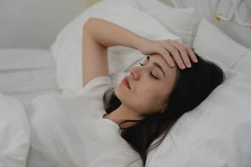 Sick woman lying in bed with eyes closed and hand on forehead, showing symptoms of headache or fever. Concept of illness, stress, fatigue, flu, migraine, and needing rest at home.