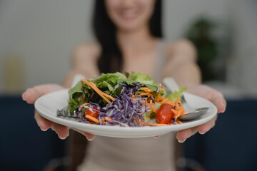 Close-up of colorful fresh salad on plate held by smiling woman, healthy meal with vegetables and...