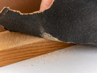 The man's hand sands the piece of wood with a piece of sandpaper.