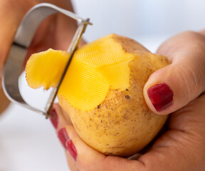 A woman peels potatoes with a vegetable peeler. The most practical and fastest way to peel...
