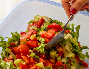 A woman's hands are preparing a salad. Salad oils, greens, and vegetables are mixed in a large bowl.